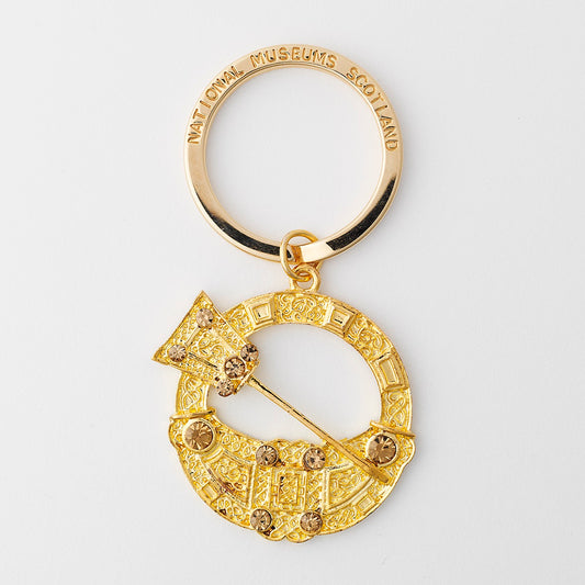 A metal key ring with a gold finish depicting the Hunterston brooch. The brooch's pin sits across an opening in the centre of the round brooch, Norse knot work and beads are features on the surrounding ring.
