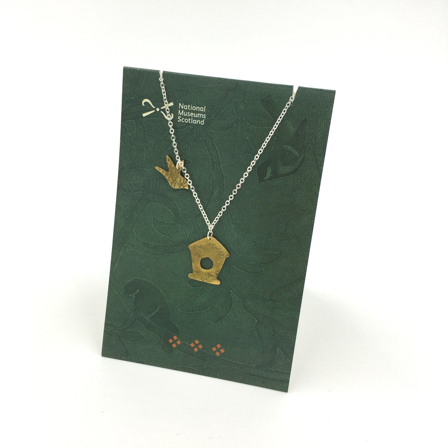 Brass chain necklace with a brass charms of a bird and a birdhouse on a green backing card against a plain white background.