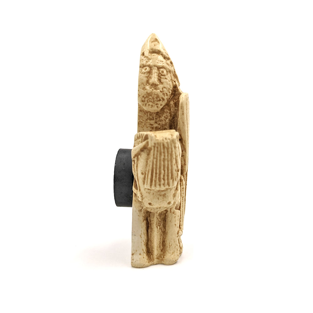 A plastic resin replica magnet of a knight Lewis chess piece. A knight on a horse facing left, the knight is wearing a pointed hat and holding a large body length shield. A side view with the knight cut in half with a round magnet attached to the back.