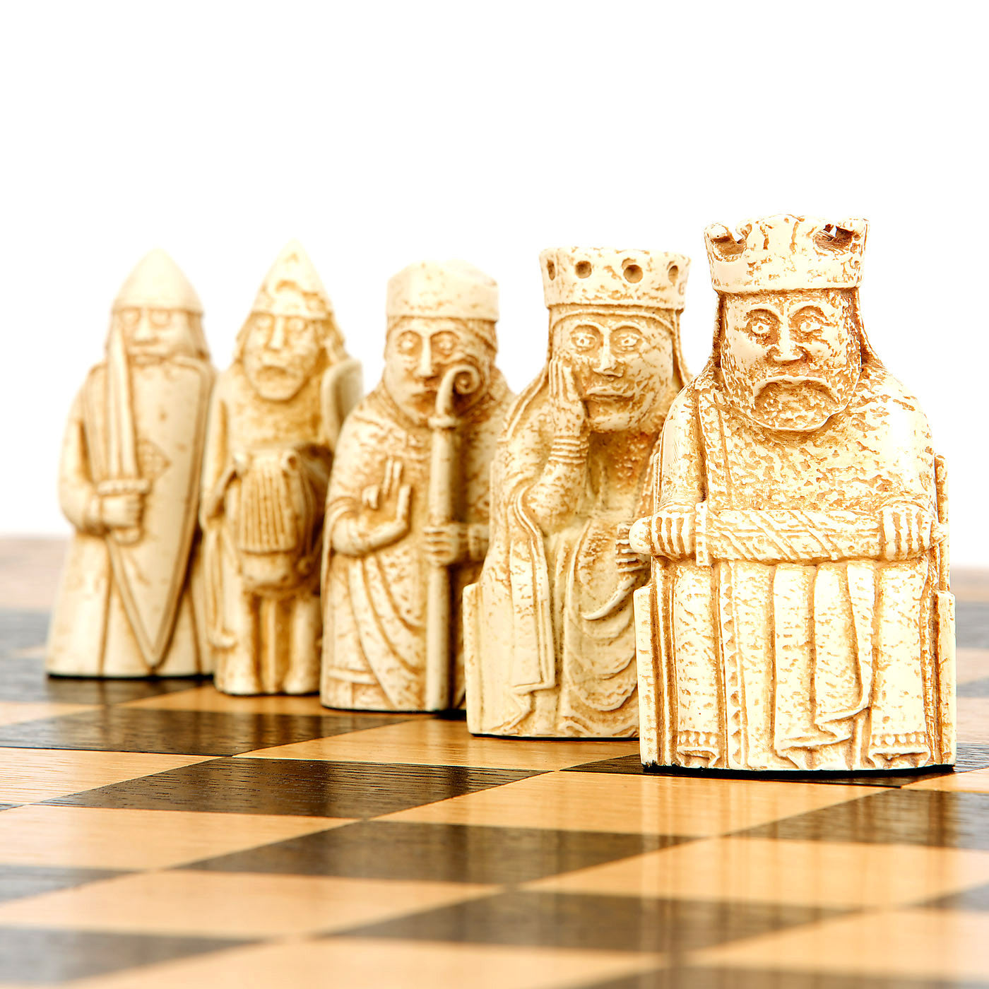 A close up photograph of a row of Lewis chess pieces on top of a natural wooden chess board. From left to right: a berserker, a knight, a bishop, a queen, a king.