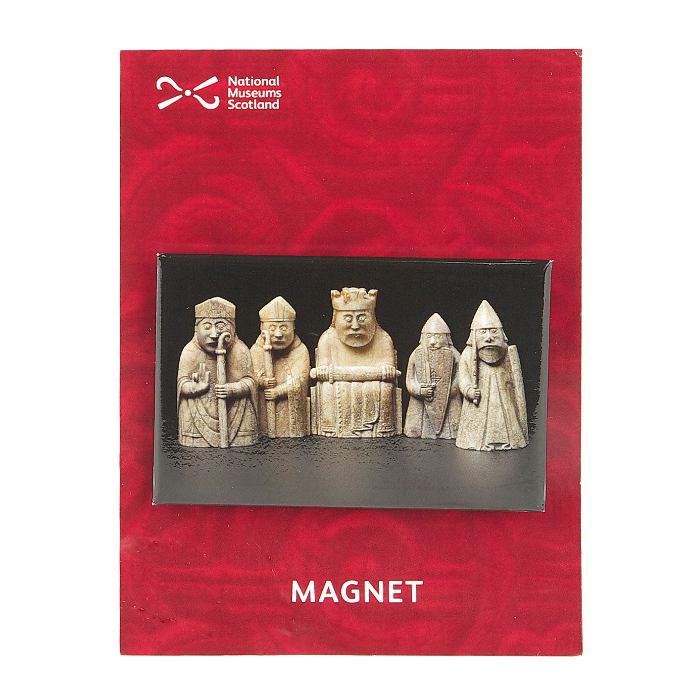 A horizontal rectangular magnet with a photograph of some Lewis chess pieces against a plain black background. The magnet is set against a red backing card that features a faint close up knot work detail.