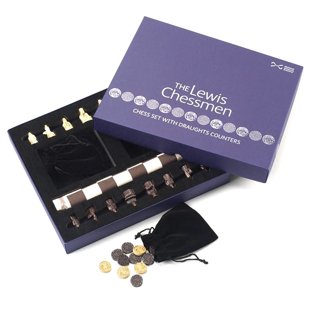 A navy blue box with the words "The Lewis Chessmen" embossed in metallic silver on the lid. The lid is open to reveal black and white chess pieces based on the Lewis chess pieces, two drawstring bags with pawns and counters inspired by Norse designs, and a cloth chess board in foam compartments.