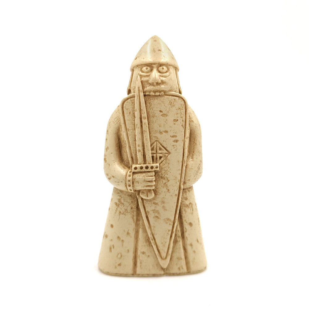 A plastic resin replica magnet of a berserker Lewis chess piece. A warrior holding a sword in front of a long shield wearing a long tunic and pointed helmet, he is biting down onto the top edge of his shield