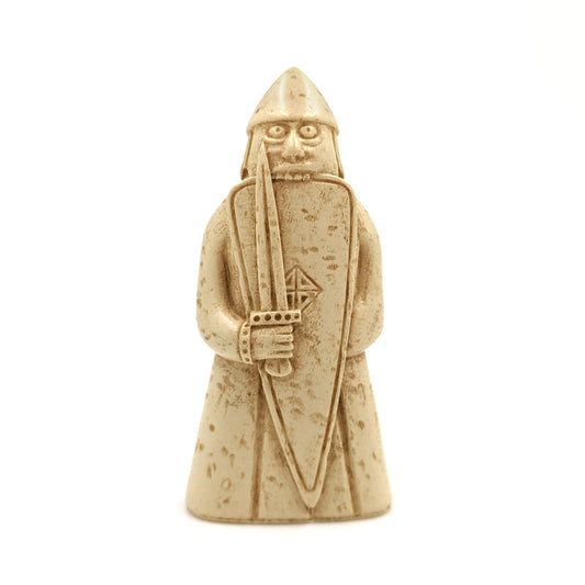 A plastic resin replica magnet of a berserker Lewis chess piece. A warrior holding a sword in front of a long shield wearing a long tunic and pointed helmet, he is biting down onto the top edge of his shield