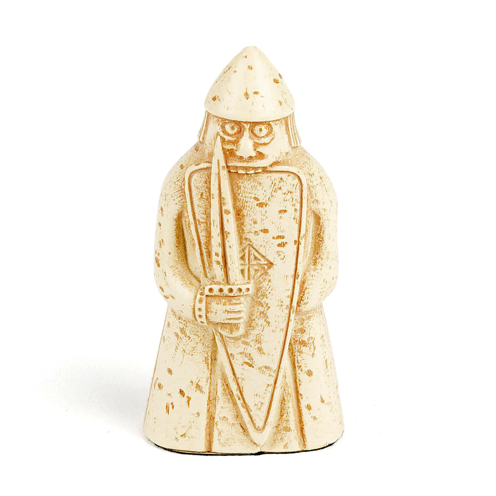 A plastic resin replica of a berserker Lewis chess piece. The berserker is wearing a long tunic and a pointed helmet, he is holding a sword and a body length shield. He has wide eyes and is biting the top edge of the shield.