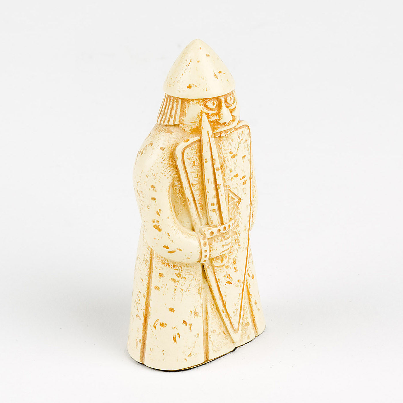 A plastic resin replica of a berserker Lewis chess piece. The berserker is wearing a long tunic and a pointed helmet, he is holding a sword and a body length shield. He has wide eyes and is biting the top edge of the shield.