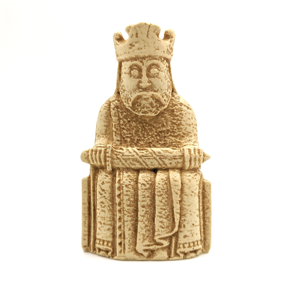 A plastic resin replica magnet of a king Lewis chess piece. The king wearing a crown and long robes sits on a throne holding a sword horizontally across his knee.
