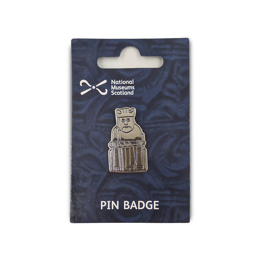A metal pin badge etched with a line illustration of a king Lewis chess piece. The pin badge is on a navy blue backing card  with a faint knot work design, the National Museums Scotland in the top left and the words "Pin Badge" across the bottom edge in white.