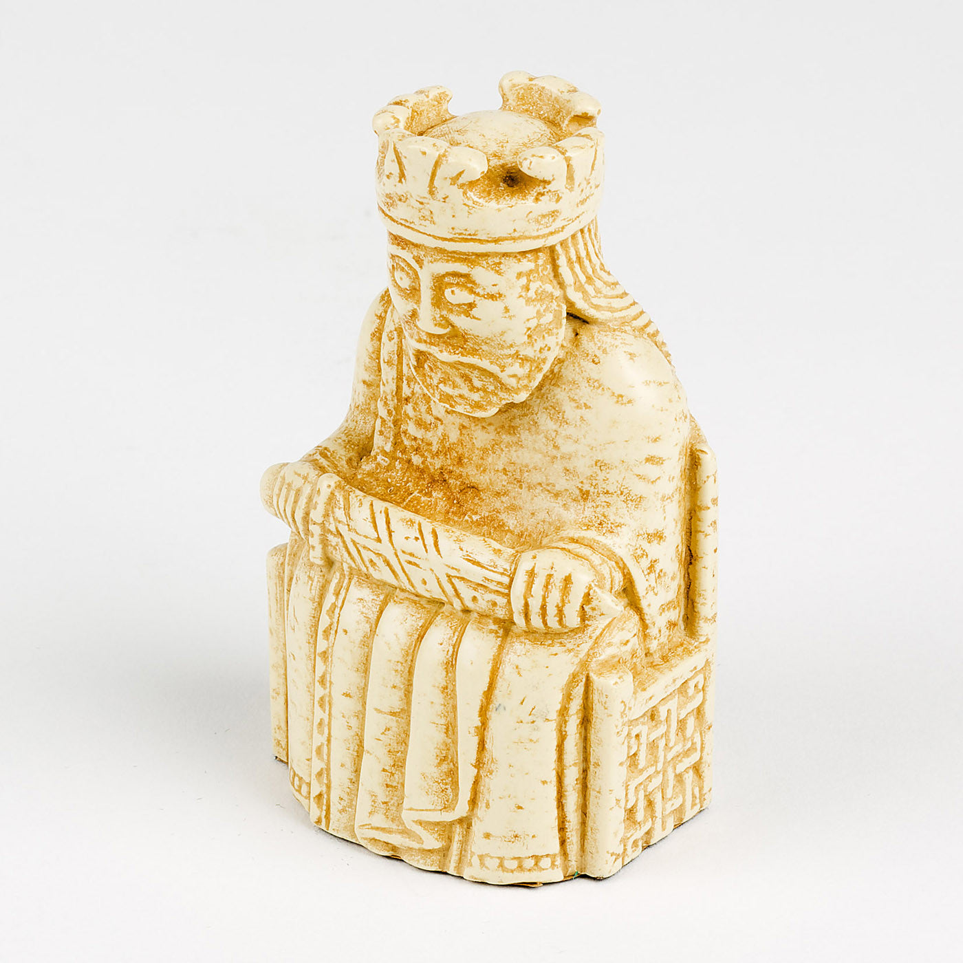 A resin replica of a king Lewis chess piece. The king is wearing long robes and a crown and is sitting on a throne decorated with knot work. He is holding a sword across his knee.