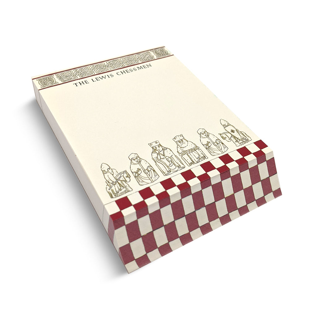 A slanted cream coloured memo pad. The top edge has a row of knot work designs with the words "The Lewis Chessmen" underneath. The bottom edge has a red chess board pattern with a row of illustrations of assorted Lewis chess pieces.