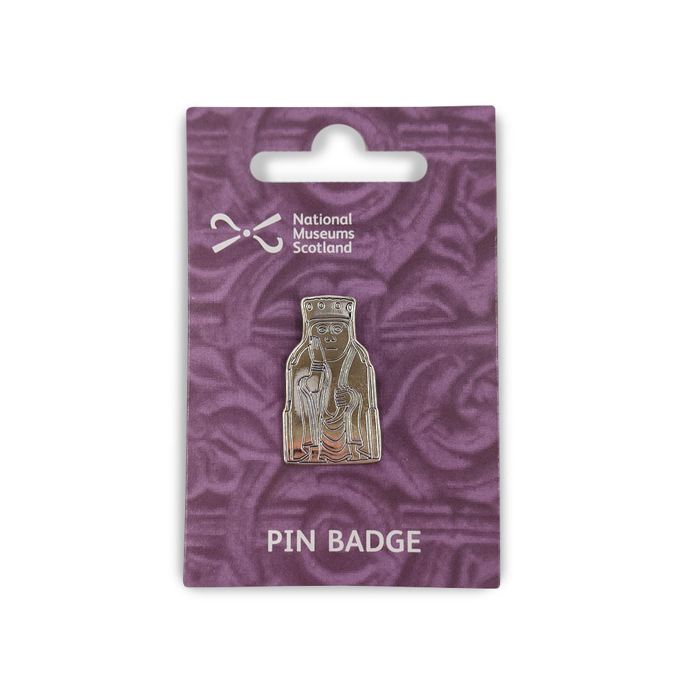 A metal pin badge etched with a line illustration of a queen Lewis chess piece. The pin badge is on a purple backing card  with a faint knot work design, the National Museums Scotland in the top left and the words "Pin Badge" across the bottom edge in white.