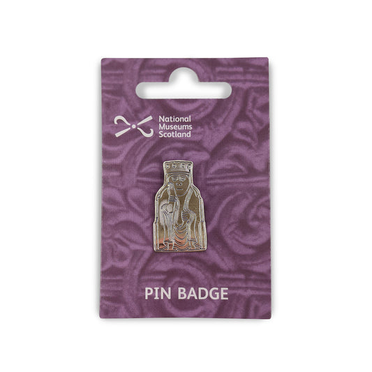 A metal pin badge etched with a line illustration of a queen Lewis chess piece. The pin badge is on a purple backing card  with a faint knot work design, the National Museums Scotland in the top left and the words "Pin Badge" across the bottom edge in white.