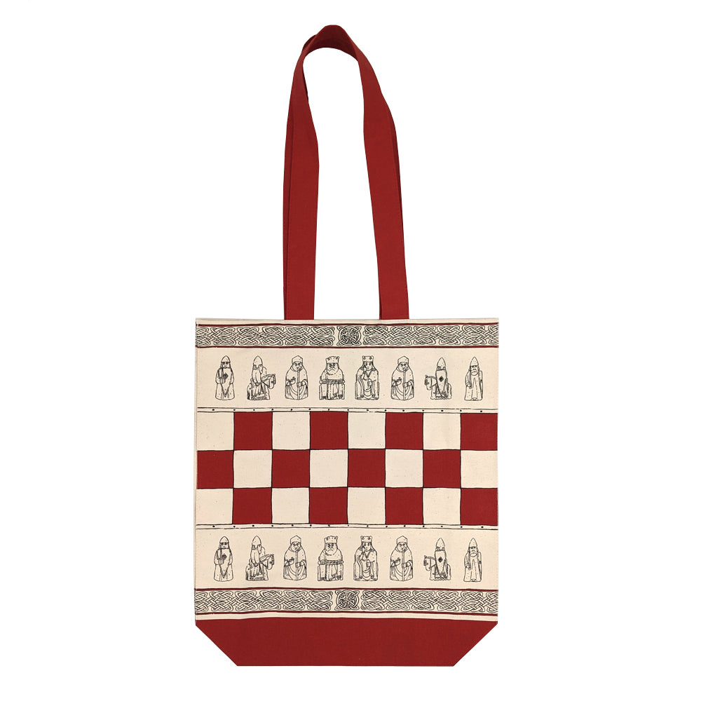 A cream coloured tote bag with a rad base and handle. The centre of the bag features a red chess board design, above and below the chess board are line illustrations of the Lewis chessmen and along the top and bottom edge of the bag are rows of knot work designs.