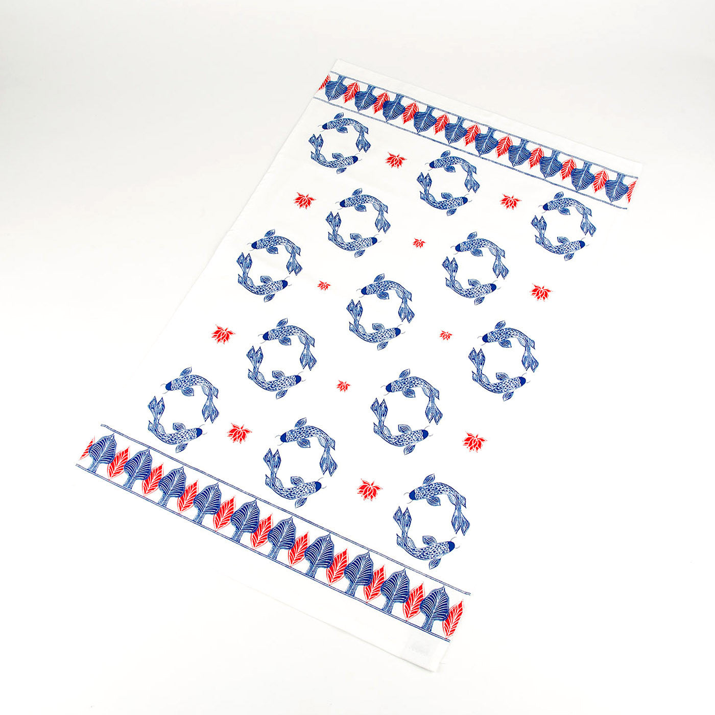 A white cotton tea towel with a repeating pattern of blue circling fish and red lotus leaves. The top and bottom edges have rows of red and blue leaves.