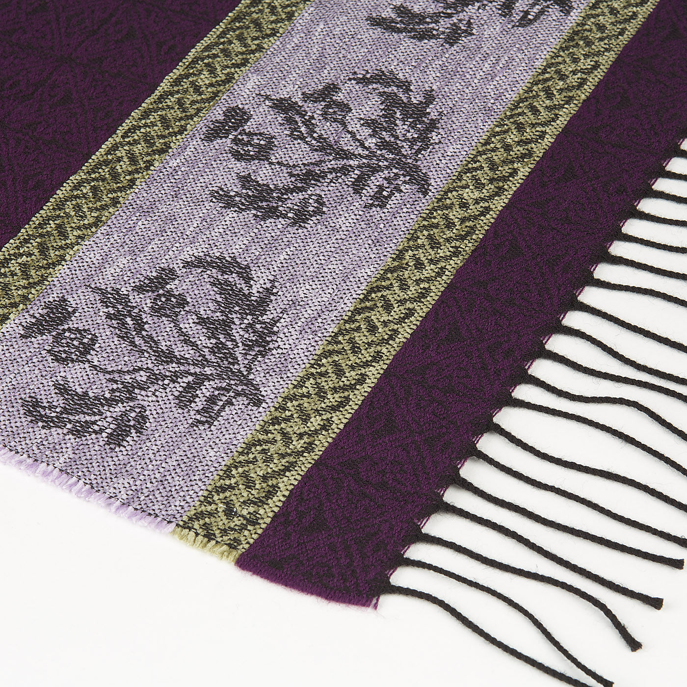 Purple tassled scarf detail with a celtic roundal and thistle pattern against a plain white background.