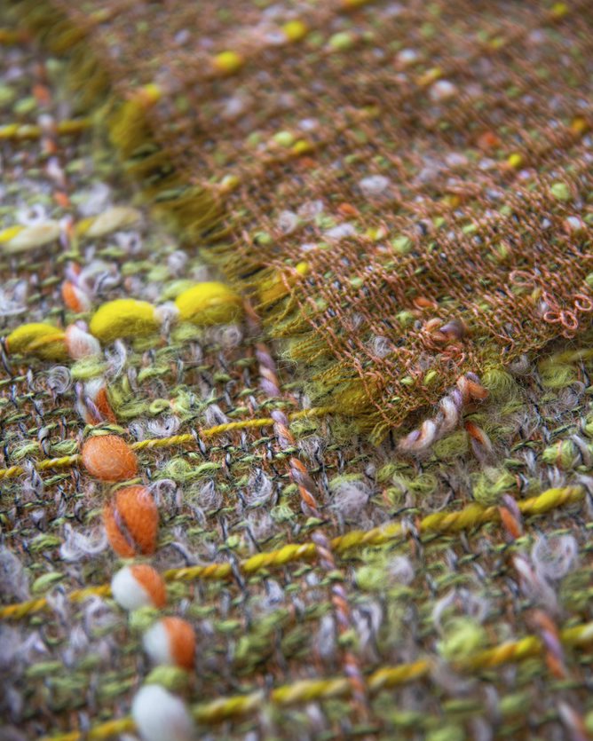 A close up photograph of some of Bernat Klein's fabric. The fabric is woven in greens, yellows and oranges.