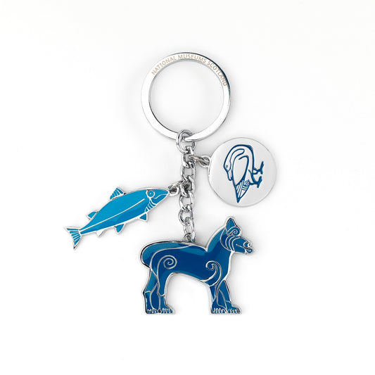 A photograph of a silver key ring with three charms of animals taken from Pictish folk art. On the left is a charm of a fish in light blue with silver detailing, in the centre is a lion in a navy blue with silver detailing, and on the right is a silver disk with a goose embossed in navy blue.