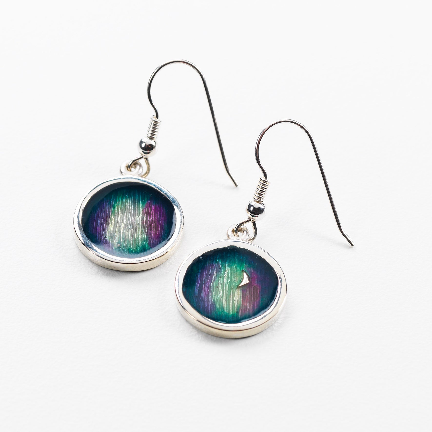 Two sterling silver round drop earrings with green, blue and purple patterns inside an outer silver ring.