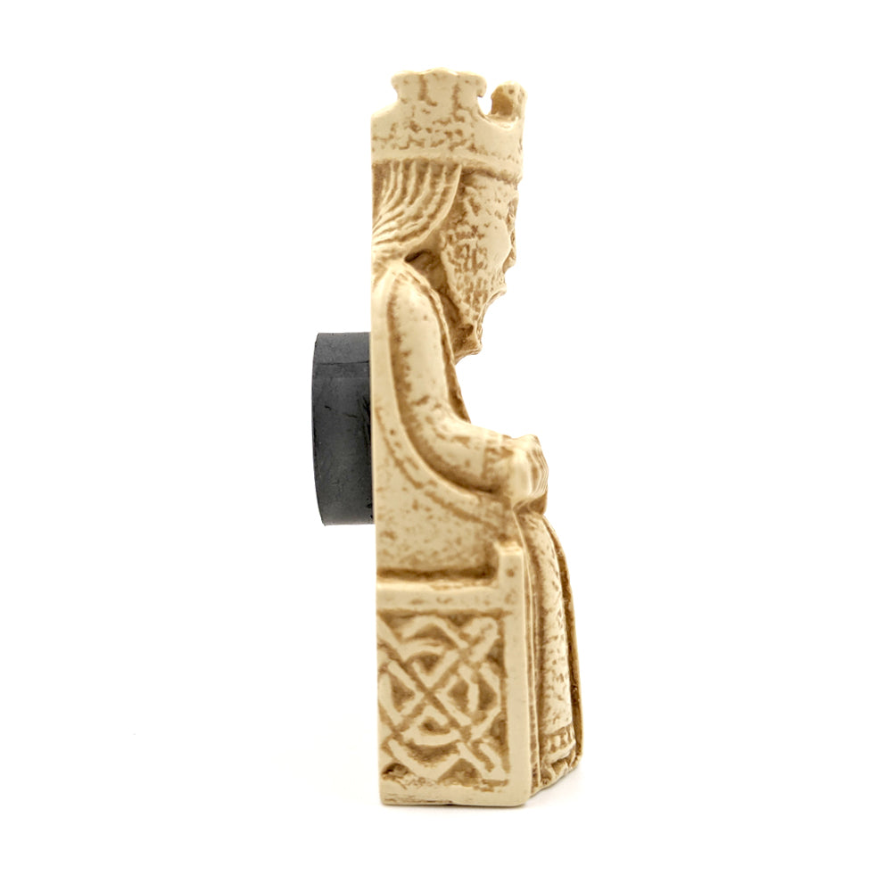 A plastic resin replica magnet of a king Lewis chess piece. The king wearing a crown and long robes sits on a throne holding a sword horizontally across his knee. A side view with the king cut in half with a round magnet attached to the back.