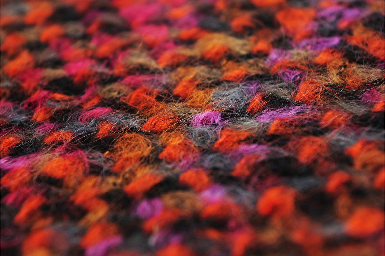 A close up photograph of some of Bernat Klein's fabric. The fabric is woven in red, black and grey.